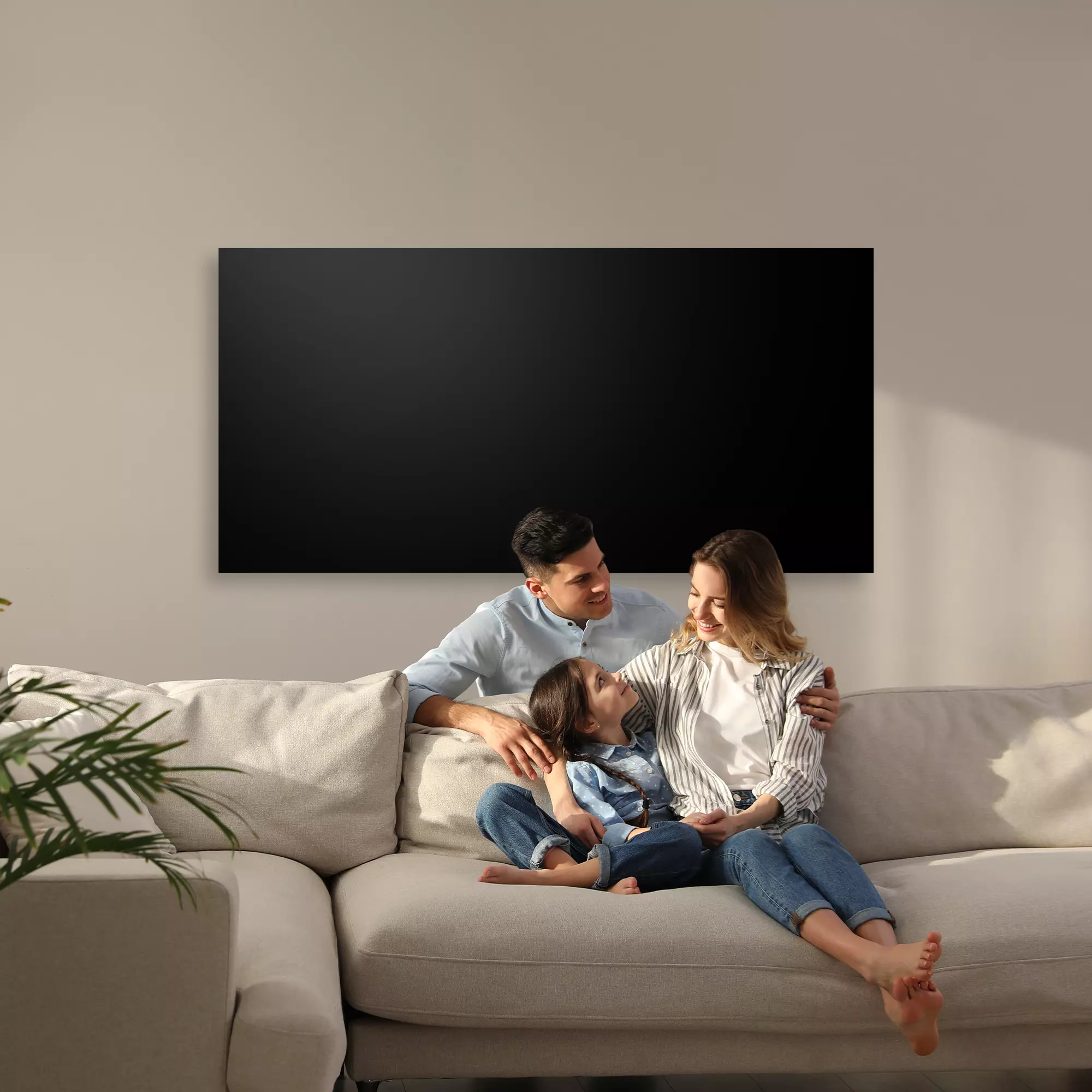 Mann, Frau und Kind kuscheln auf dem Sofa, schwarze Infrarotheizung an Wand